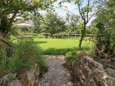 A garden with a stone path leading to a grassy area with a table and umbrella and two chairs at Little Freestone in Carew