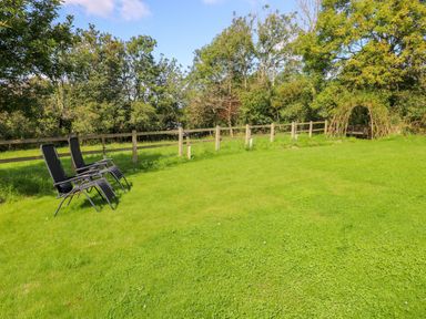 A grassy garden with two black chairs near a wooden fence and a seating area with an archway in the background at Little Freestone in Carew