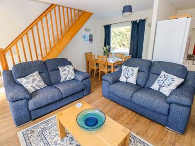 A living room with two blue sofas a wooden coffee table and staircase with a dining area in the background at Little Freestone in Carew