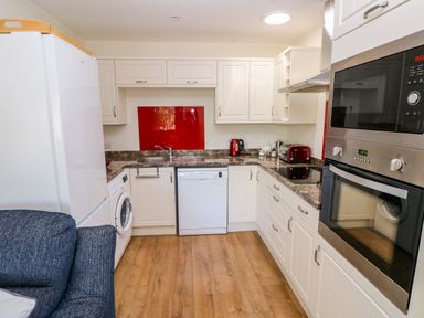 A kitchen with white cabinets wooden floor dishwasher washing machine and red kitchen appliances at Little Freestone in Carew