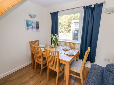A dining area with a wooden table set for six next to a window with blue curtains at Little Freestone in Carew