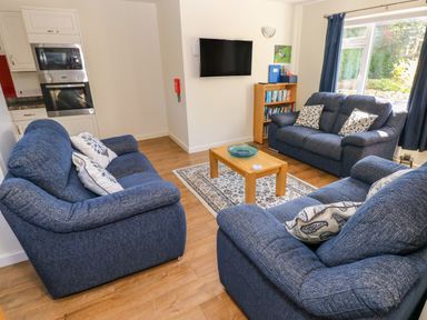 A living room with blue sofas a wooden coffee table a wall-mounted television and a bookshelf at Little Freestone in Carew