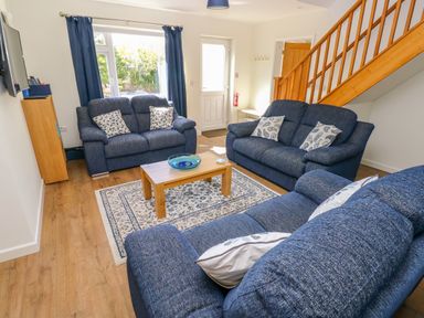 A living room with blue sofas a wooden coffee table and staircase at Little Freestone in Carew