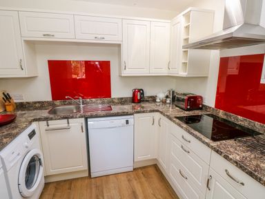A kitchen with white cabinets brown countertops red backsplash and appliances at Little Freestone in Carew