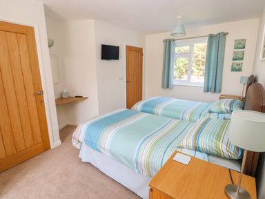 A bedroom with two single beds striped bedding wooden doors and a wall-mounted tv at Little Freestone in Carew