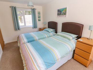 A bedroom with two single beds with striped bedding and wooden bedside tables with lamps at Little Freestone in Carew