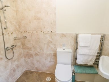 A bathroom with a shower, toilet, towel rack with white towels, and a green bath mat at Little Freestone in Carew