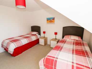 A bedroom with two single beds with red plaid bedding and matching red lamps on bedside tables at Little Freestone in Carew
