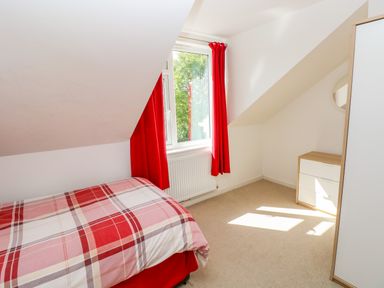 A bedroom with a bed a window with red curtains and a chest of drawers at Little Freestone in Carew