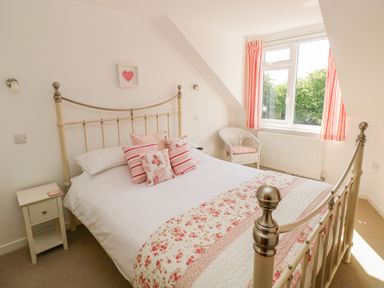 A bedroom with a metal bed frame and floral bedding and cushions next to a window with pink curtains at Little Freestone in Carew