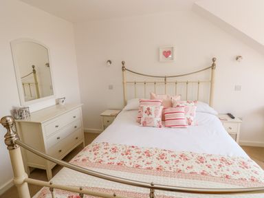 A bedroom with a metal bed and floral pillows next to a dresser with a mirror at Little Freestone in Carew