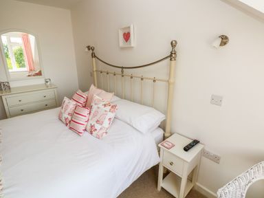 A bedroom with a bed with floral and striped pillows a dresser with a mirror and a nightstand with a remote at Little Freestone in Carew
