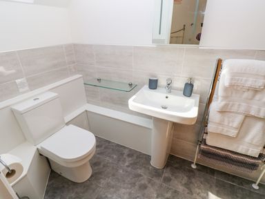 A bathroom with a toilet sink glass shelf and towel rack at Little Freestone in Carew