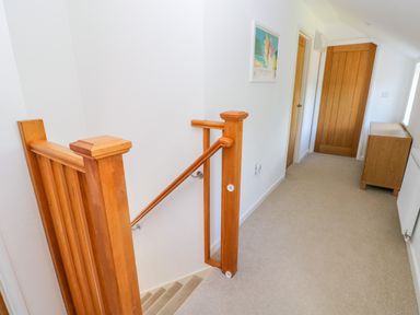 A hallway with wooden staircase railing a wooden door and a wooden cabinet at Little Freestone in Carew