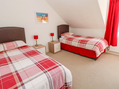 A bedroom with two single beds red plaid bedding and red lamps at Little Freestone in Carew