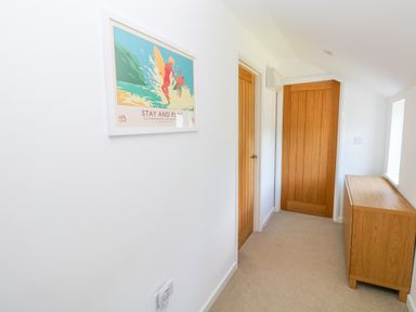 A hallway with two wooden doors a wooden cabinet and a framed surfing poster on the wall at Little Freestone in Carew
