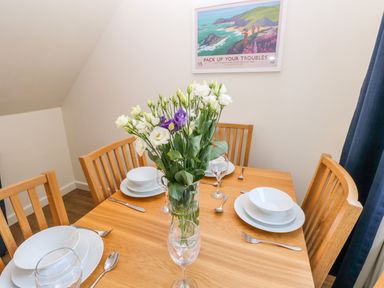 A dining table set with white dishes glassware and a vase of flowers at Little Freestone in Carew