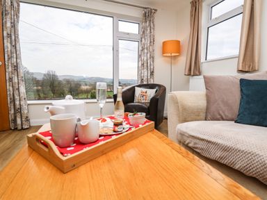 A living room with a wooden table holding a tray with tea set and a small bottle near a window showing an outdoor landscape at Gwynant in Pontrhydfendigaid