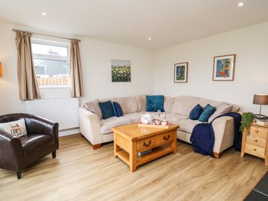 A living room with a beige corner sofa and blue cushions a wooden coffee table and a brown armchair with a cushion at Gwynant in Pontrhydfendigaid