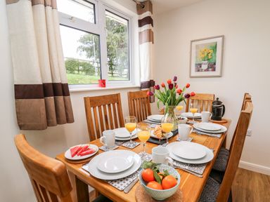 A dining room with a wooden table set with plates glasses and cups a vase of tulips and a bowl of oranges at Gwynant in Pontrhydfendigaid