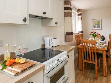 A kitchen with a stove cutting board with fruit and drinks and a dining table with chairs and breakfast setup at Gwynant in Pontrhydfendigaid