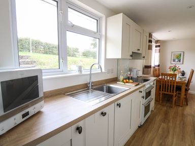 A kitchen with a wooden countertop a sink a microwave a stove and a dining table with chairs at Gwynant in Pontrhydfendigaid