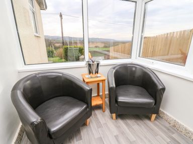 Two black armchairs with a small wooden table holding a metal bucket with a bottle and glasses in a corner with large windows at Gwynant in Pontrhydfendigaid