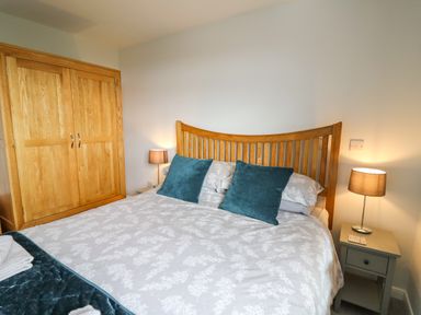 A bedroom with a wooden bed frame and wardrobe two bedside tables with lamps and cushions on the bed at Gwynant in Pontrhydfendigaid