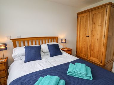 A bedroom with a wooden bed frame bedside tables lamps and a wooden wardrobe at Gwynant in Pontrhydfendigaid