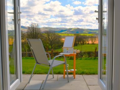 A chair and small table outside on a patio overlooking grassy fields and hills at Gwynant in Pontrhydfendigaid