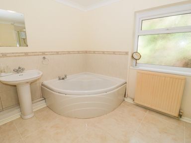 A bathroom with a corner bathtub pedestal sink window radiator and a small mirror on the windowsill at Glan Gors in Llanerchymedd