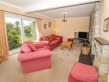 A living room with pink sofas a coffee table a television and stone fireplace at Glan Gors in Llanerchymedd