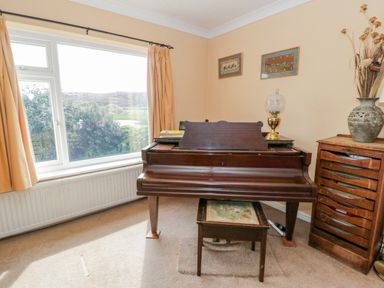 A piano with a stool and lamp next to a window with curtains in a room at Glan Gors in Llanerchymedd