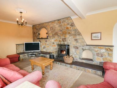 A living room with a stone wall fireplace a wooden coffee table a television and pink upholstered sofas at Glan Gors in Llanerchymedd
