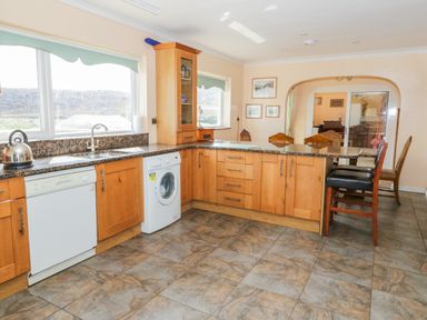 A kitchen with wooden cabinets dishwasher washing machine granite countertops and high chairs at Glan Gors in Llanerchymedd