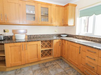 A kitchen with wooden cabinets a granite countertop a window and tiled floor at Glan Gors in Llanerchymedd