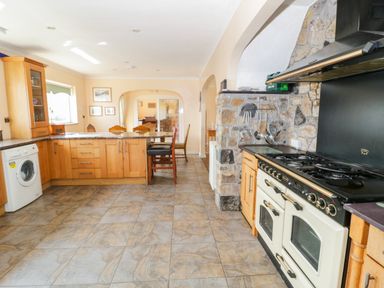 A kitchen with wooden cabinets a washing machine a stove with an extractor fan and a dining table with chairs at Glan Gors in Llanerchymedd