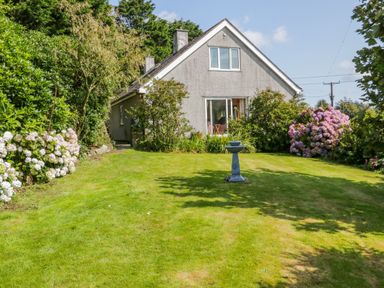 A house with a sloped roof surrounded by a garden with lawn flowers and a birdbath at Glan Gors in Llanerchymedd