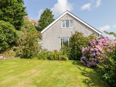 A garden with bushes and a flowerbed in front of a two-story house at Glan Gors in Llanerchymedd