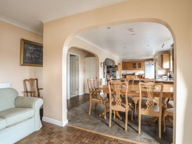 A dining area with a wooden table and chairs next to a kitchen with wooden cabinets and a refrigerator at Glan Gors Llanerchymedd