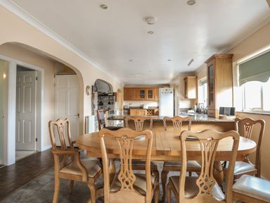 A kitchen and dining area with wooden chairs and table a stone fireplace and kitchen cabinets at Glan Gors in Llanerchymedd