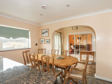 A dining area with a wooden table and six chairs near a window and an archway at Glan Gors in Llanerchymedd