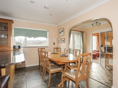 A dining room with a wooden table and chairs near a window and archway at Glan Gors in Llanerchymedd