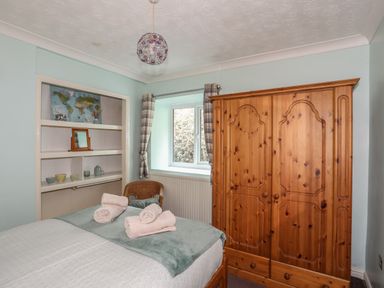 A bedroom with a wooden wardrobe a bed with towels on it a window with plaid curtains and built-in shelves with decorative items at Glan Gors Llanerchymedd