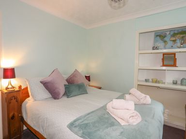 A bedroom with a bed with pillows and folded towels on it and shelves with decorative items at Glan Gors in Llanerchymedd