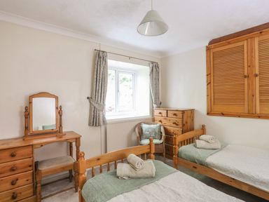 A bedroom with two single beds a wooden dresser a chair and a window at Glan Gors in Llanerchymedd