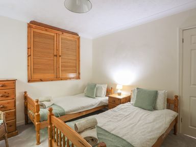 A bedroom with two single wooden beds with white and green bedding a wooden chest of drawers a wooden nightstand with a lamp and a window with wooden shutters at Glan Gors in Llanerchymedd