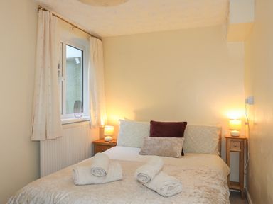A bedroom with a bed with pillows and rolled towels two bedside tables with lamps and a window with curtains at Glan Gors in Llanerchymedd