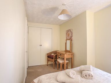 A bedroom with a bed and rolled towels a wooden dressing table and chair beside a built in closet at Glan Gors in Llanerchymedd