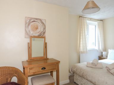 A bedroom with a wooden dressing table mirror wicker chair bed with rolled towels and window with curtains at Glan Gors in Llanerchymedd